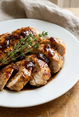 A white plate holding sliced chicken breast covered in a rich balsamic fig glaze.