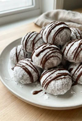 A close-up of white snowball cookies with dark chocolate drizzles on a plate.