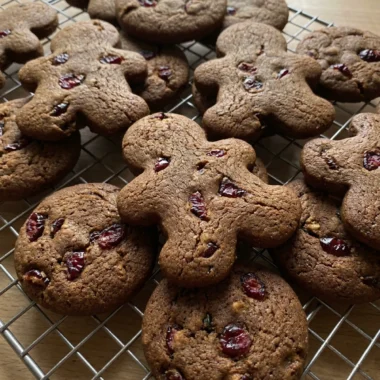 A close-up of a gingerbread man cookie with visible red cranberry pieces inside.