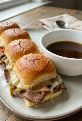 Finished French dip sliders with melted cheese, served hot from the oven with au jus.