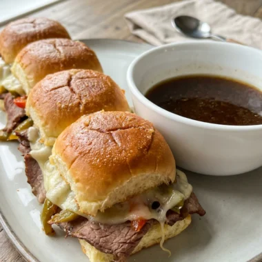 Finished French dip sliders with melted cheese, served hot from the oven with au jus.