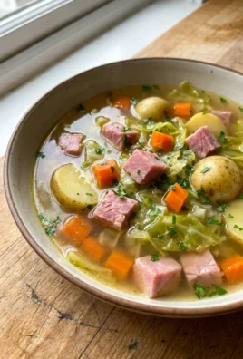 A close-up of a white bowl filled with ham, cabbage, and potato soup.