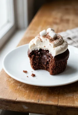 A single hot chocolate cupcake with tall white frosting on a small white plate.
