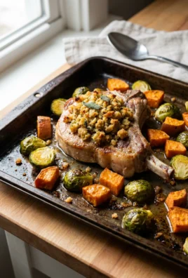 Close-up of a cooked pork chop with a golden stuffing crust next to roasted vegetables.
