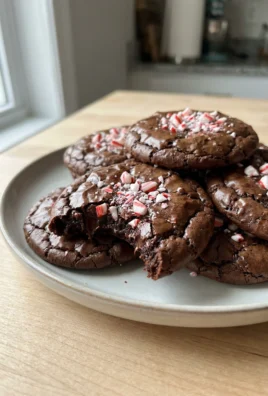A hand holding a peppermint brownie cookie that has been broken in half to show the fudgy interior.