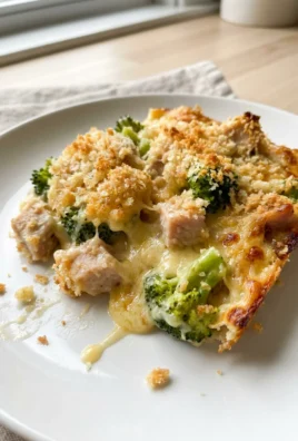 A serving of bubbly turkey divan casserole on a white plate with a fork.
